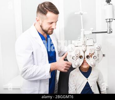 Optometrist doctor checks the young girl's eyesight on the pforopter. If the girl has poor eyesight, the doctor will give a prescription for glasses Stock Photo