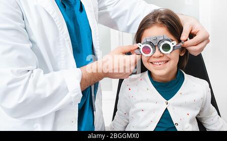Mixed race girl wearing optometrist trial frame at ophthalmology clinic. doctor assistance select glasses for treatment of vision Stock Photo