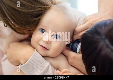 Doctor pediatrist examining childs ear with otoscope. Mom holding baby with hands. Medicine, healthcare ,pediatry and people. Children healthcare and Stock Photo