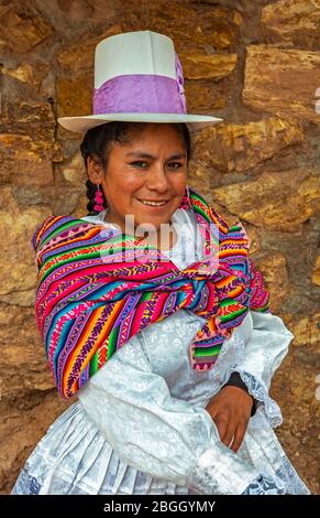 Smiling Peruvian Quechua indigenous Woman in traditional clothing from the Maras people: white dress, high profile hat and woolen scarf. Maras, Peru. Stock Photo
