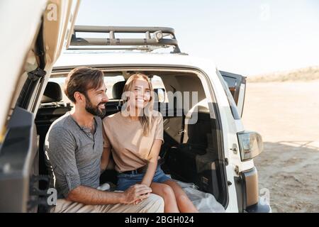 Lovely young happy couple sitting in the back of their car at the beach, embracing