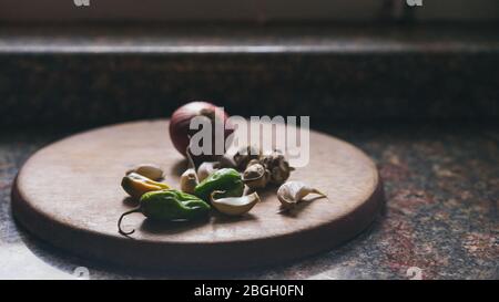 A set of traditional local Asian spices for Indian cuisine: garlic, onion, ginger, chili on a round wooden chopping board, dark marble background Stock Photo