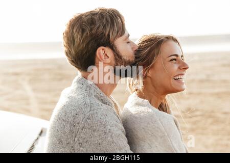 Close up of a happy young couple in love embracing while leaning on a car at the sunny beach, kissing