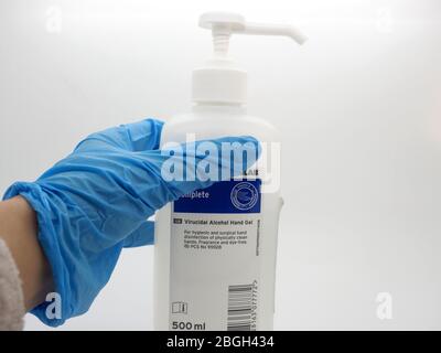 A Hand, Wearing A Blue Disposable Glove Picking Up A Bottle Of Sanitiser Gel, London, UK Stock Photo