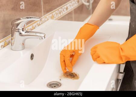 Woman cleaning company eliminates clogging of hair in sink, cleans tile Stock Photo