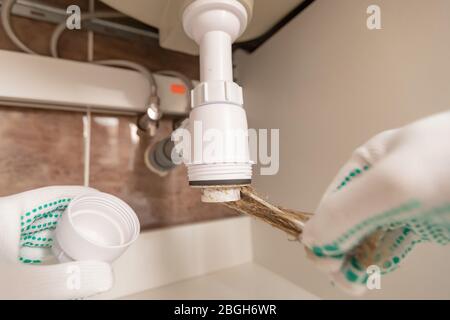 Professional male plumber eliminates blockage in siphon of sink drain pipe Stock Photo
