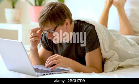 Young man with glasses is working from home during Coronavirus or Covid-19 quarantine. Man using laptop for work during self-isolation. Stock Photo