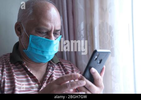senior man with mask using smart phone indoor  Stock Photo