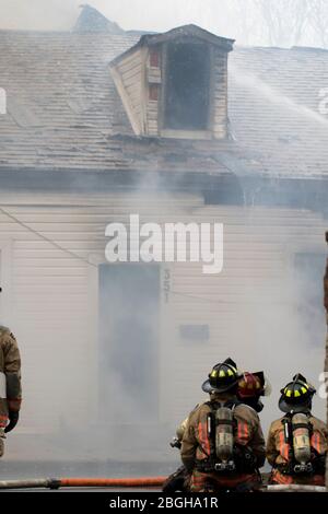 Ontario, Canada April 20 2020:Putting out roof fire with water hose. Firefighters douse burning building to get large fire under control. Crime scene Stock Photo