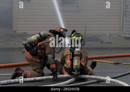 Two firefighters holding hose putting out house fire. Fighting large structure fire. Stock Photo