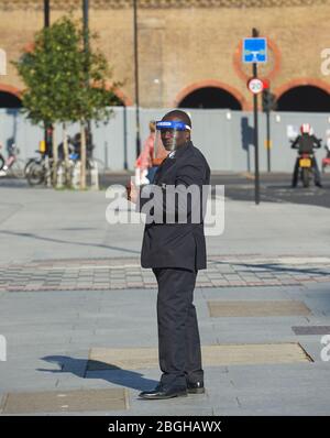 London, UK. 21st April 2020.    A Security Guard in a full face mask marshals  the queue outside a supermarket in London.  Credit: Thomas Bowles/Alamy Live News Stock Photo
