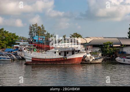 Thailand - January 31, 2018: An old rusty ship stands near the shore on a river. Near small speed boats. Horizontal. Stock Photo