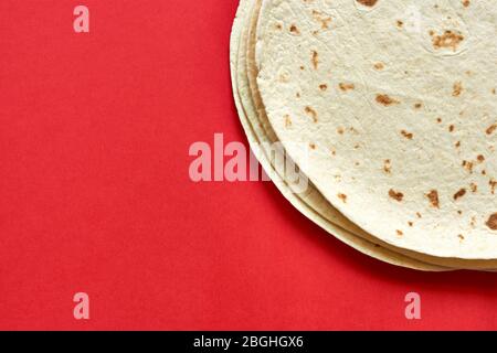 Tortillas on red background. A pile of  baked blank corn tortilla wraps on a color background with copy space. Top view or flat lay. Stock Photo