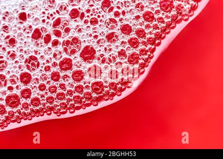 Macro image of foam bubbles from soap or shampoo in wave form on a shiny red glass background with copy space. Stock Photo