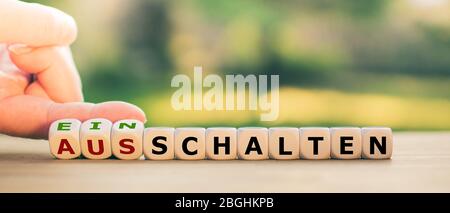 Hand turns dice and changes the German word 'Ausschalten' ('turn off') to 'Einschalten' ('turn on'). Stock Photo