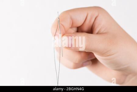 Detail of hand holding needle with thread on white background Stock Photo