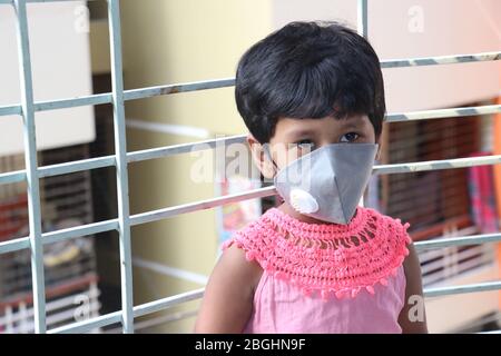 Passing boring time due to Corona virus Outbreak. Lock down and school closures. A School girl with face mask watching outside through the window. Stock Photo