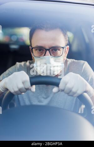 Close up of driver in protective mask with hands in rubber gloves on steering wheel, covid-19 protection from bacteria and virus infection. Stock Photo