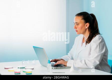 Female scientist working in a laboratory with laptop and Petri dish investigating the coronavirus. Microbiological laboratory. Stock Photo