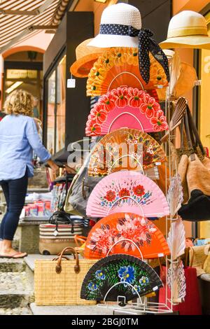 BELLAGIO, LAKE COMO, ITALY - JUNE 2019: Colourful fans and hats on display outside a shop in Bellagio on Lake Como. Stock Photo