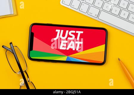 A smartphone showing the Just Eat logo rests on a yellow background along with a keyboard, glasses, pen and book (Editorial use only). Stock Photo