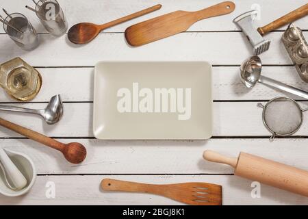 A rectangular glass white bowl lies on a wooden table. Stylish kitchen utensils forming the background are spread out around. Stock Photo