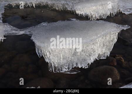 Close-up of candled ice block during spring melt on Yukon River shoreline, with rocks in background Stock Photo