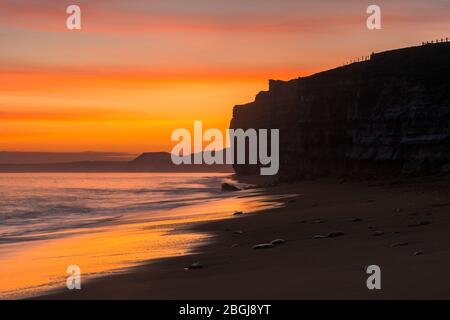 Burton Bradstock, Dorset, UK.  21st April 2020.  UK Weather.  View along the cliffs towards West Bay and Golden Cap as the sky glow orange shorty after sunset at Hive Beach at Burton Bradstock in Dorset as the settled weather set to continue this week with rising temperatures.  Picture Credit: Graham Hunt/Alamy Live News Stock Photo