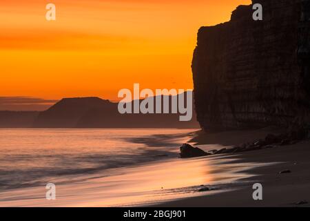 Burton Bradstock, Dorset, UK.  21st April 2020.  UK Weather.  View along the cliffs towards West Bay and Golden Cap as the sky glow orange shorty after sunset at Hive Beach at Burton Bradstock in Dorset as the settled weather set to continue this week with rising temperatures.  Picture Credit: Graham Hunt/Alamy Live News Stock Photo