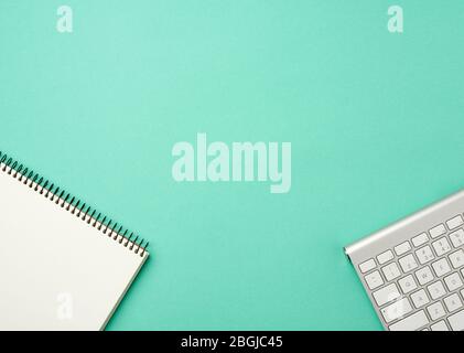 white wireless aluminum keyboard and open notebook with blank white sheets on a green background, top view, workplace Stock Photo