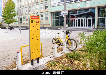 BRATISLAVA (SLOVAKIA) – OCTOBER 06 2019: Yellow public bikes locked in docking station in front Faculty of Management of Comenius University Stock Photo