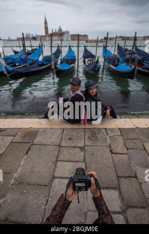 woman taking picture of couple with gondola's in Venice Stock Photo
