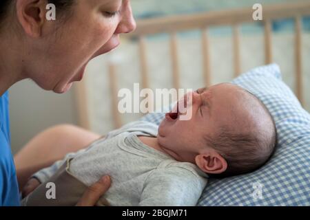 Mother with mouth open imitating yawning baby at home Stock Photo