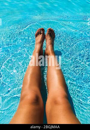 female legs in the blue water of the pool Stock Photo