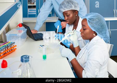 Two African scientists, technical assistants or graduates in lab coats and gloves perform PCR testing of patient samples in modern test laboratory. RT Stock Photo