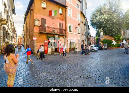 A female tourist uses her cell phone as other tourists walk by the shops and cafes in a small piazza in the Trastevere district of Rome, Italy. Stock Photo