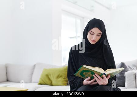 young traditional muslim woman reading Quran on the sofa before iftar dinner during a ramadan feast at home Stock Photo