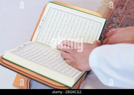 young arabian muslim man in traditional clothes reading holy book Quran on the praying carpet before iftar dinner during a ramadan feast at home Stock Photo
