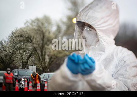 A nurse changes out gloves while New Jersey National Guard Airmen direct traffic at a COVID-19 Community-Based Testing Site at the PNC Bank Arts Center in Holmdel, N.J., March 23, 2020.  The testing site, established in partnership with the Federal Emergency Management Agency, is staffed by the New Jersey Department of Health, the New Jersey State Police, and the New Jersey National Guard. This image was captured with a tilt-shift lens. (U.S. Air National Guard photo by Master Sgt. Matt Hecht) Stock Photo