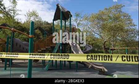 Bi-lingual caution tape ropes of a California playground closed down due to Covid-19 social distancing regulations. Stock Photo