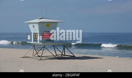 A lifeguard tower sits on an empty beach, with a sign stating that the beach is closed due to Covid-19. Stock Photo