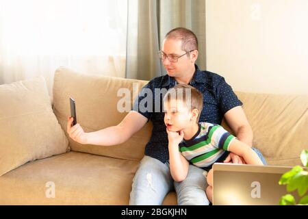 Father and son communicate online by phone with relatives or friends. Online communication, remote communication. Stock Photo