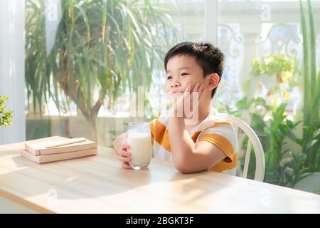 A asian boy drinking milk while sitting at desk after doing homework. E-learning and education concept. Stock Photo
