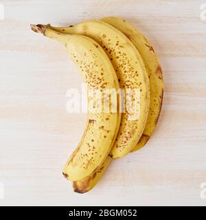 Ripe bananas with brown spots on bright white wooden table Stock Photo
