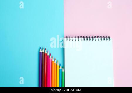 Color pencils and notebook on color background. Stock Photo