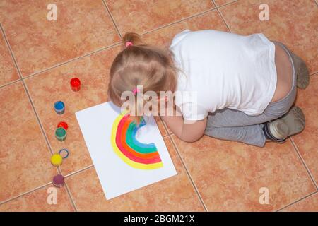Kid painting rainbow at home during pandemic coronavirus quarantine. Stock Photo