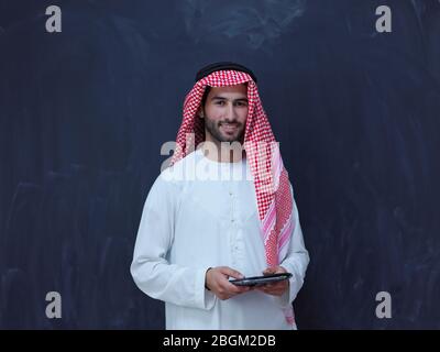 young arabian muslim businessman using tablet computer wearing hijab clothes in front of black chalkboard Stock Photo