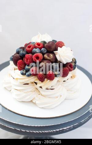 Meringue Pavlova cake with chocolate sauce, whipped cream and fresh cherries, strawberries, blueberries. Stock Photo
