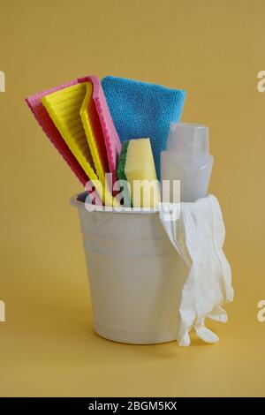 Container with cleaning items against yellow background Stock Photo