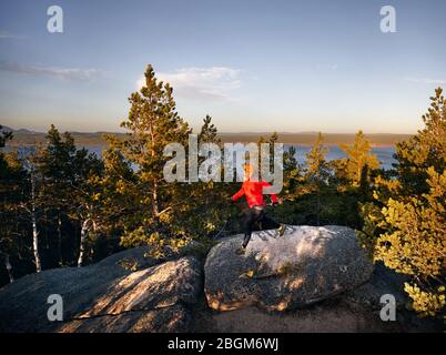 Bearded man in red shirt running in the pine forest at sunset. Trail running concept Stock Photo